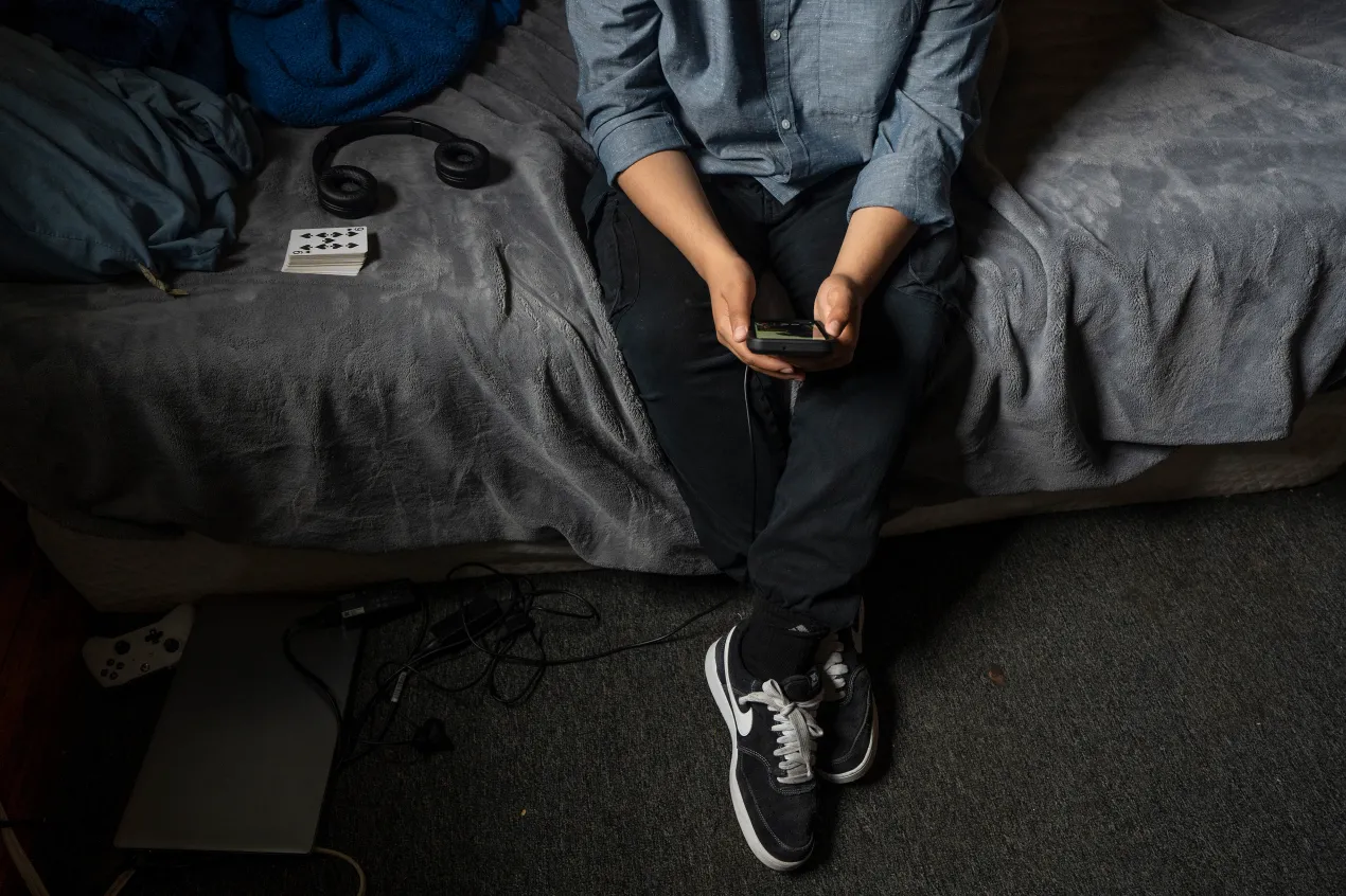 A person holds a smartphone as they sit on a bed