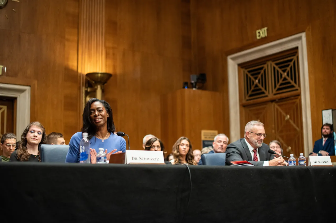 A wide shot of a Senate hearing room. Erica Schwartz and Sean Kaufman sit next to each other at the witness table.
