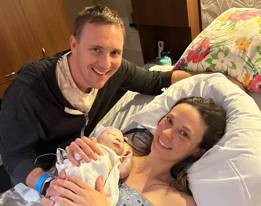 A photo of Emilie Solomon in a hospital bed. She holds her newborn son in her arms. Her husband, Justin, is by the bed.