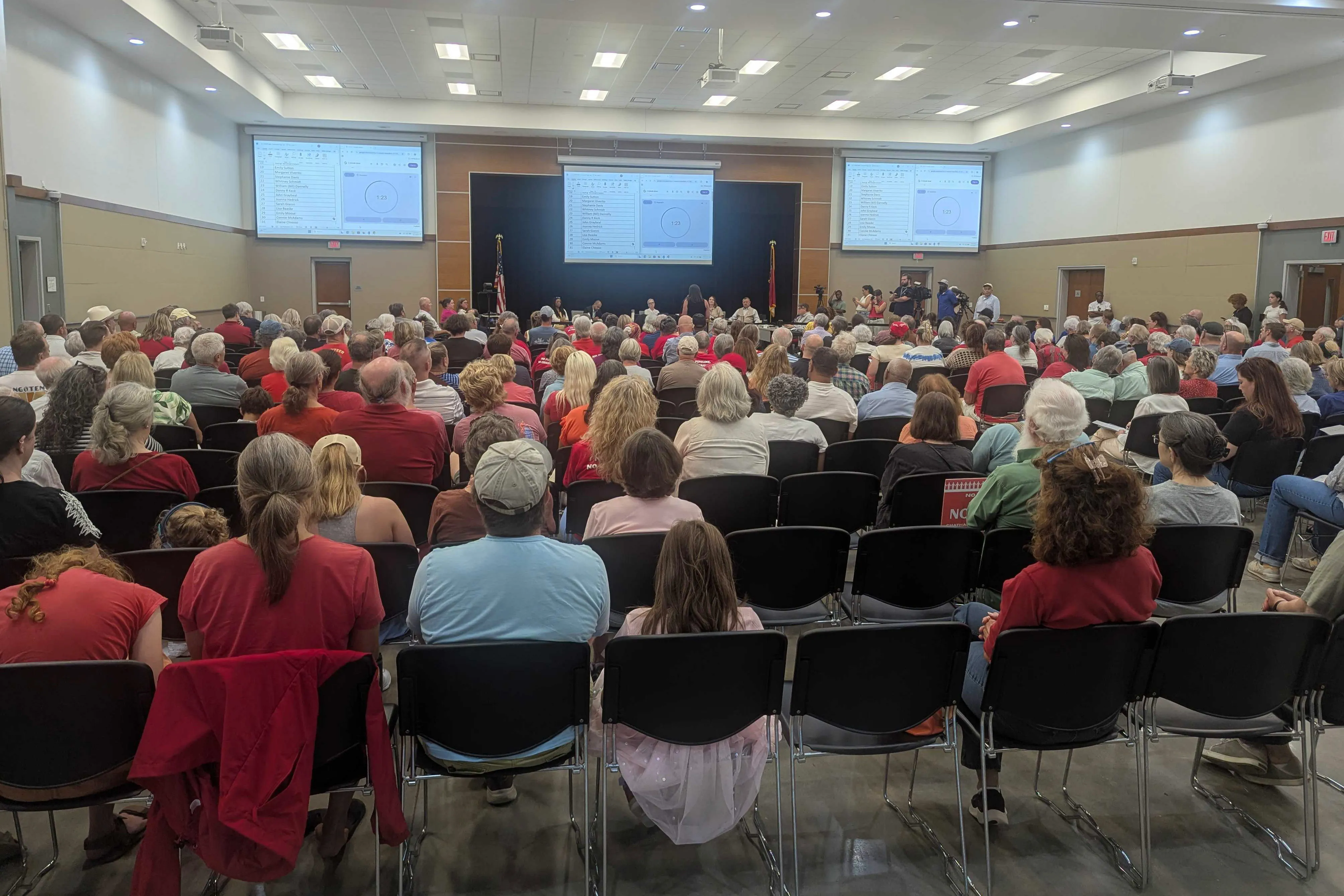 A photo taken from the back of a Board of Commissioners meeting room. The seats are mostly filled with attendees wearing red shirts.